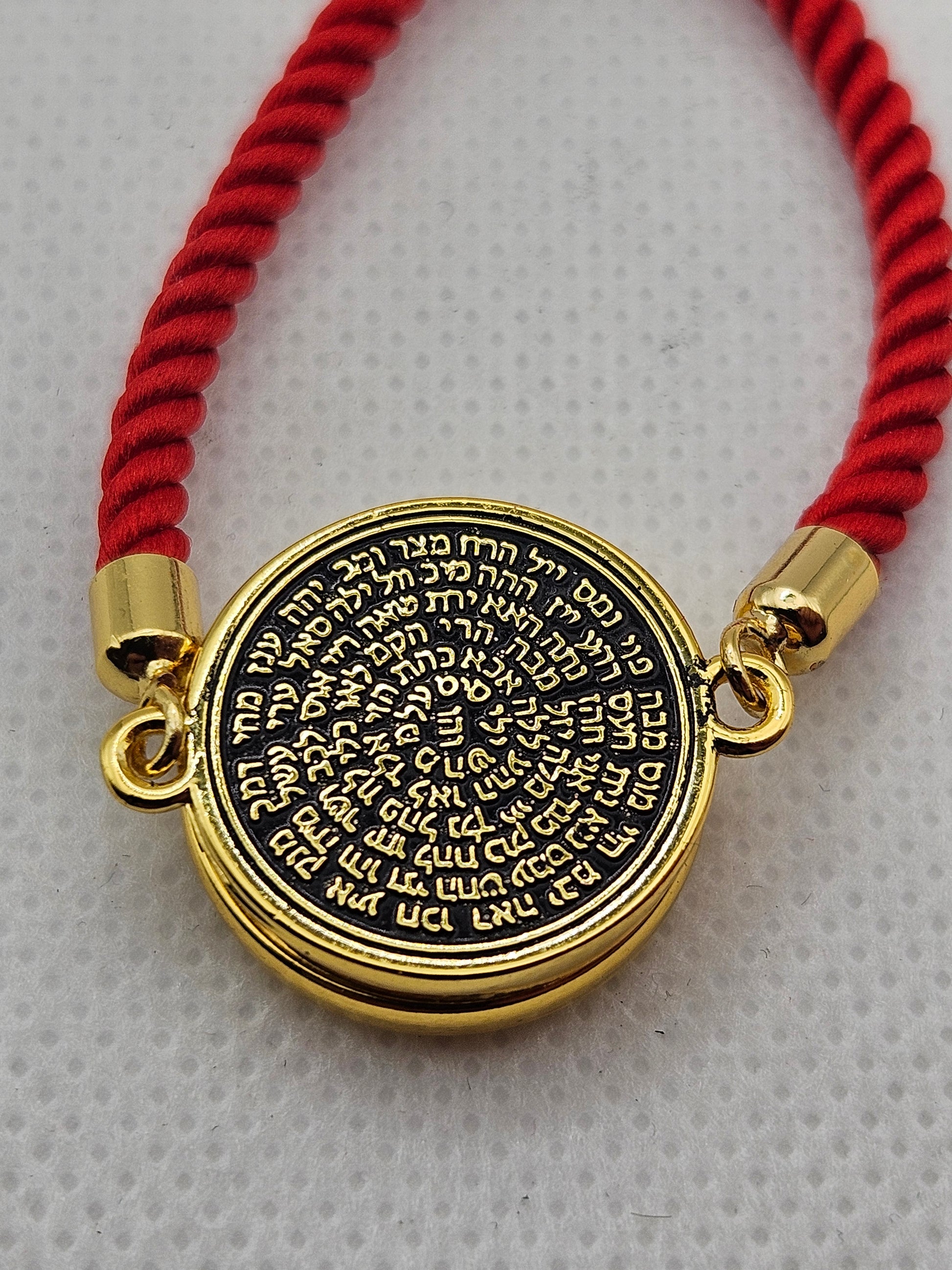 Gold pendant with Hebrew text on a red string bracelet against a gray background