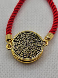 Gold pendant with Hebrew text on a red string bracelet against a gray background