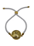 White bracelet with gold circular pendant on a light gray background