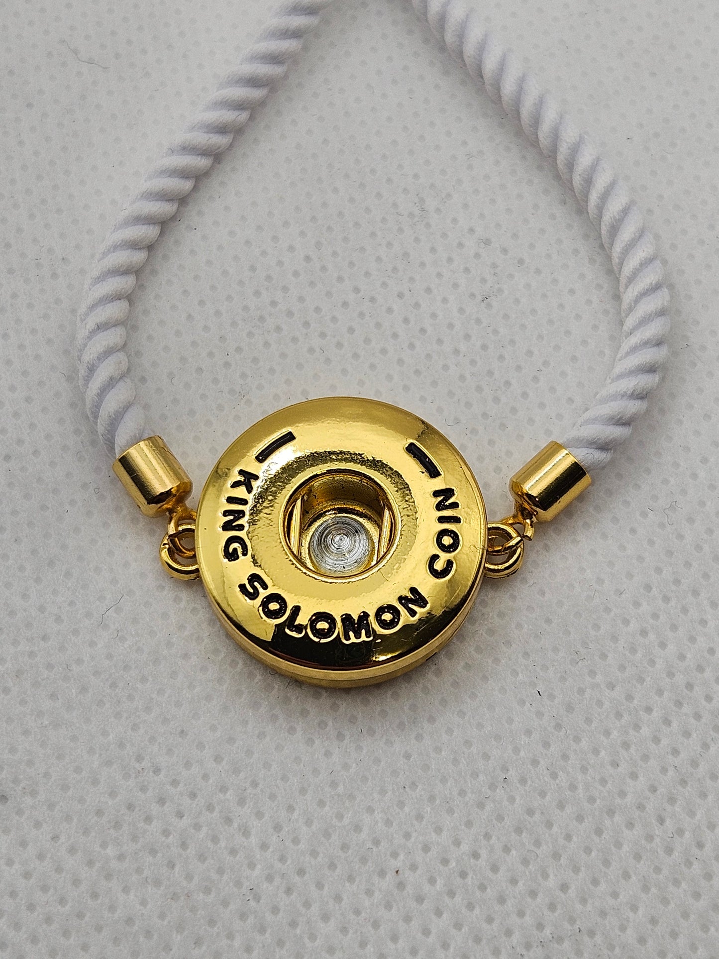 Gold button necklace with a white cord on a textured gray background